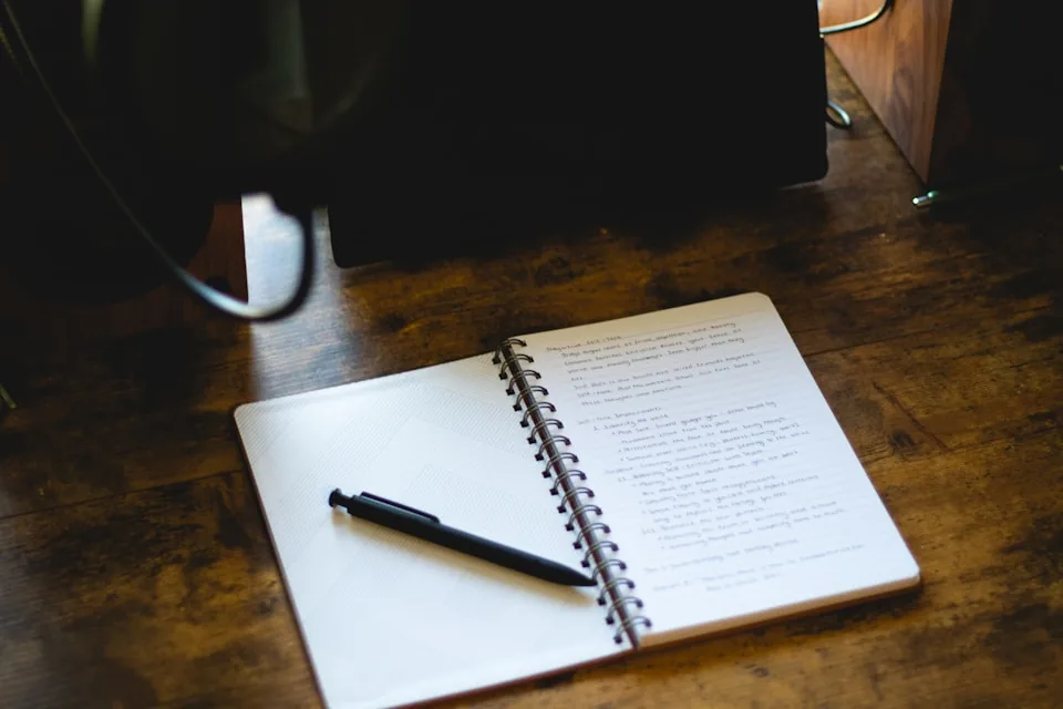 Un carnet ouvert et un stylo posés sur un bureau en bois.